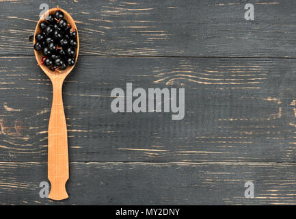 Bird cherry in spoon on empty wooden background, top view
