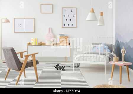 Pink table and grey wooden armchair in girl's bedroom interior with mockup of empty poster Stock Photo