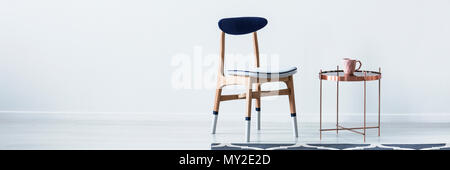 Blue and white wooden chair standing by metal end table with pastel pink mug in bright room interior with place for your cupboard Stock Photo