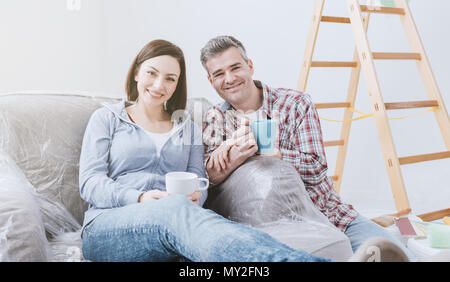 Happy couple doing home renovations in their new house, they are having a coffee break and relaxing Stock Photo