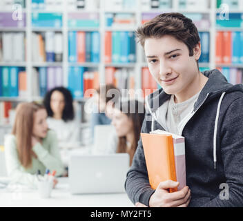 Confident young student posing with books, group of students in the background Stock Photo