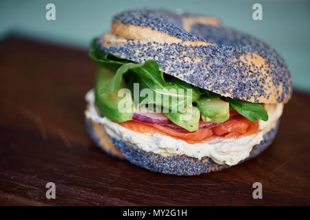 Closeup of a delicious salmon and cream cheese poppy seed bagel with vegetables sitting on a wooden serving board Stock Photo