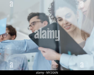 Young business team working in the office, two women on the foreground are checking paperwork on a clipboard Stock Photo