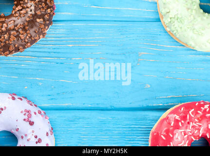 Four donuts with different glaze located in the corners on a blank wooden background Stock Photo