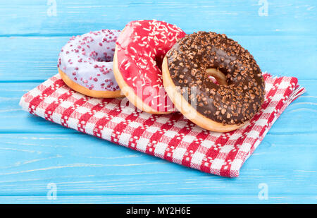 Three donut with multicolored glaze on a towel and a blue table Stock Photo