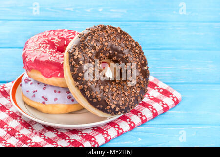 Three donut with multicolored glaze in a saucer on a blue wooden background Stock Photo