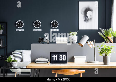 Laptop on wooden desk with lamp and plant in modern home office interior with poster Stock Photo