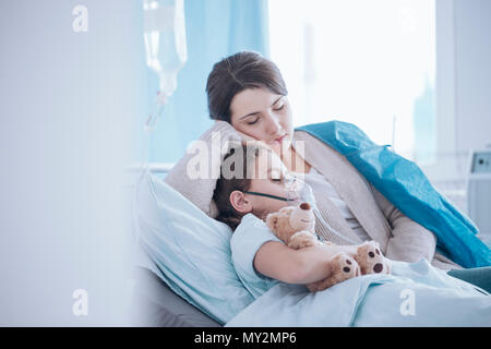 Mother taking care of sick daughter with oxygen mask and teddy bear Stock Photo