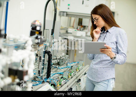 Portrait of young female student of robotics stands in a lab with digital tablet Stock Photo