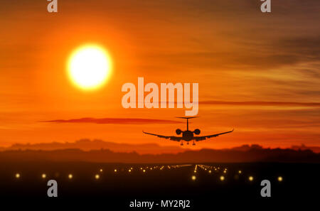 Airplane silhouette landing at the airport during sunset. Sun, shape of private jet plane and flashing runway lights. Stock Photo