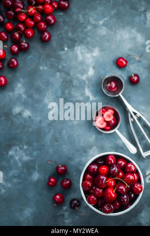 Fresh cherries on a concrete background with a small metal bucket and an ice cream spoon. Making summer dessert concept flat lay with copy space.