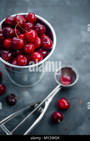 Cherries with an ice cream spoon and metal bucket on a grey concrete background, Summer berries concept with copy space. Neutral color tones still lif