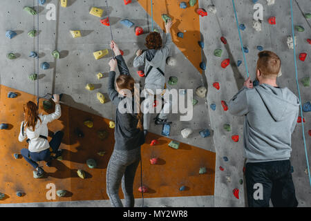 Two little kids climbing a wall at gym and their mother and father holding securing ropes Stock Photo