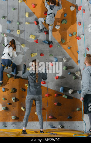 Full-length shot of two little kids climbing a wall at gym and their mother and father holding securing ropes Stock Photo