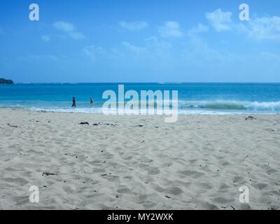 Beautiful beach day with tourists taking a stroll in the sand, the ocean with waves & a blue sky with white clouds on the Caribbean island Martinique Stock Photo