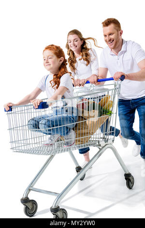 happy young parents carrying cute redhead daughter in shopping cart isolated on white Stock Photo