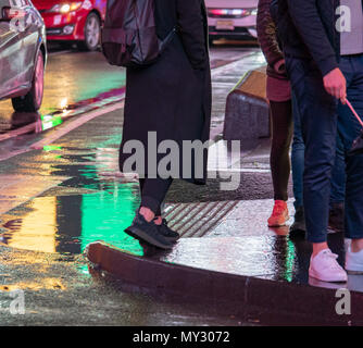 A woman walking through Times Square, New York City in rain with puddle reflection on ground of neon lights Stock Photo