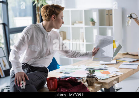 stylish fashion designer with lot of paperwork sittin on work desk Stock Photo