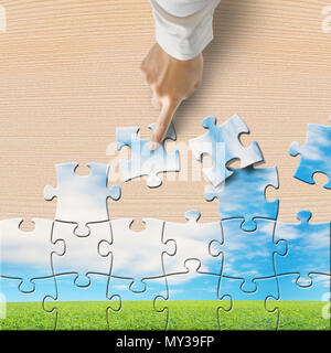 Hand pushing puzzles to assembly with beautiful landscape on wooden table Stock Photo