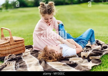cute little siblings having fun together while resting on plaid at picnic Stock Photo