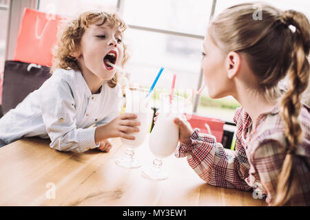 adorable happy little children drinking milkshakes with straws in cafe Stock Photo