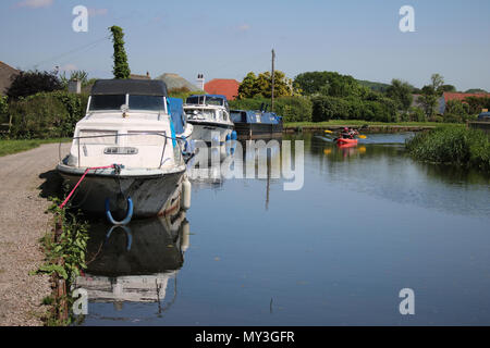 View along the Lancaster canal at Hest Bank in Lancashire, England with boats moored alongside the towpath and a red canoe on the water. Stock Photo