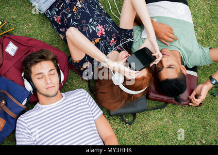 Friends lying on grass, using virtual reality simulator and listening to headphones Stock Photo