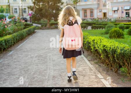Rear view of young schoolgirl in uniform with backpack going to school Stock Photo