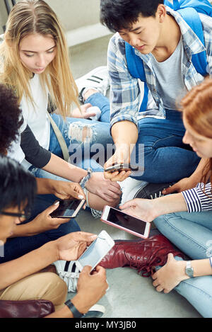 Group of students sitting together on floor, looking at smartphones Stock Photo