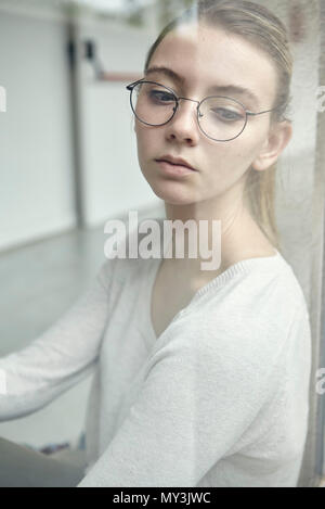 Young woman looking through window in thought, portrait Stock Photo