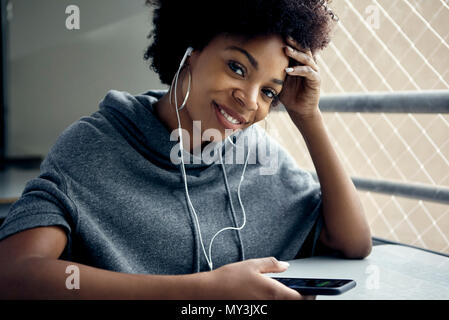 Young woman using smartphone and earphones, smiling, portrait Stock Photo