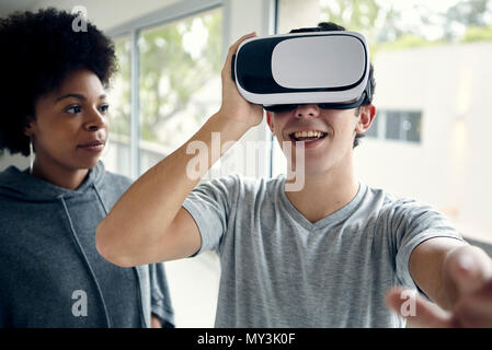 Young man using virtual reality simulator with friend Stock Photo