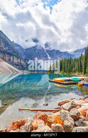 Reflective Moraine Lake at Lake Louise near Banff in the Canadian Rockies, with canoes nearby and heavy clouds descending on the Valley of Ten Peaks i Stock Photo