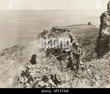 8 25 1944  marines manning a field howitzer blast a Japanese nest in a cave from the edge of a sheer cliff on Tinian Stock Photo