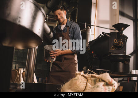 young coffee roaster with metal bucket in hands working in coffee shop Stock Photo