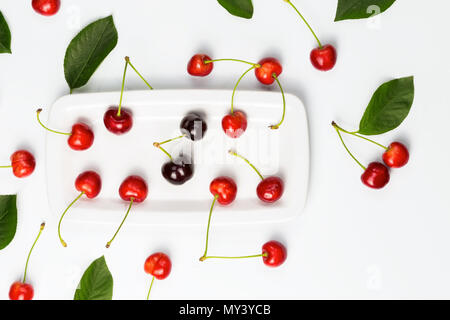 Ripe cherry berries and cherry leaves on white plate isolated top view. Useful as food presentation background. Stock Photo