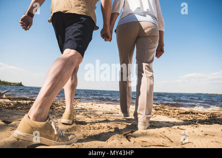 Cropped shot of senior couple holding hands and walking on sandy beach Stock Photo