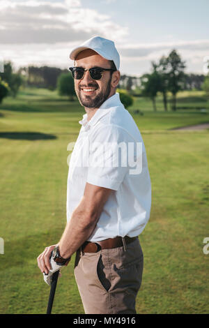 Handsome man in sunglasses holding golf club and smiling at camera Stock Photo