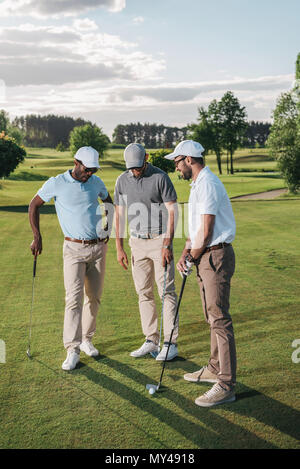 Multiethnic group of golfers holding clubs and talking while standing ...