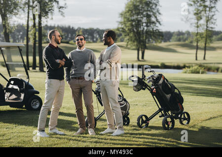 multiethnic golfers with golf clubs talking and spending time together on golf course Stock Photo