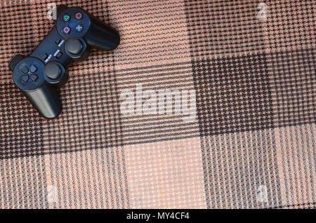 Close-up photo of a black plastic wireless game controller on a background of checkered fabric cover. Game joystick. Let's go play a video game Stock Photo