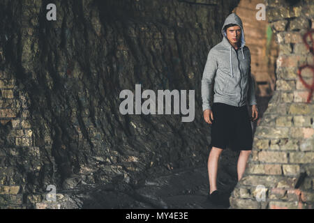 young man in hoodie looking at camera while standing on ruins Stock Photo