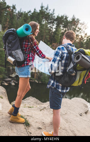 active couple with backpacks looking at map near mountain lake