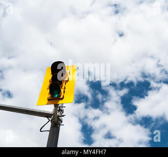 Traffic signal on metal pole with green light lit in yellow structure against partly cloudy sky. Stock Photo