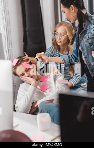 women glue stickers on sleeping man at office Stock Photo