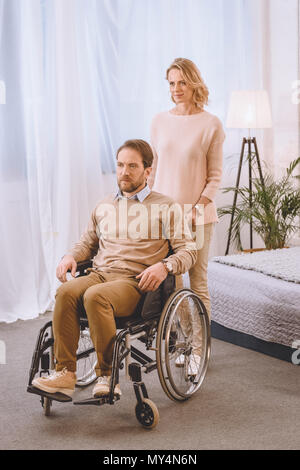 husband on wheelchair and wife looking away in bedroom Stock Photo