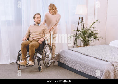 husband on wheelchair and wife in light bedroom Stock Photo