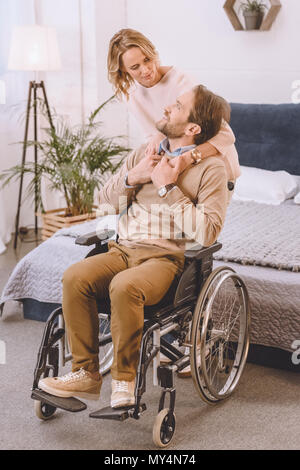 wife hugging husband on wheelchair from back in bedroom Stock Photo