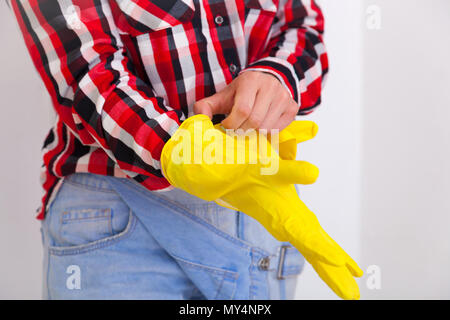 Сlose up of young woman  in jeans and plaid shirt hands wearing protective rubber yellow gloves. Women's housework and safety, housekeeping concept Stock Photo