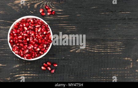 White bowl filled with pomegranate seeds on an empty table, top view Stock Photo